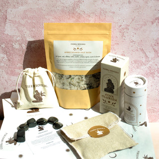 Collection of wellness products including a bag, stones, and boxes on a textured pink surface.